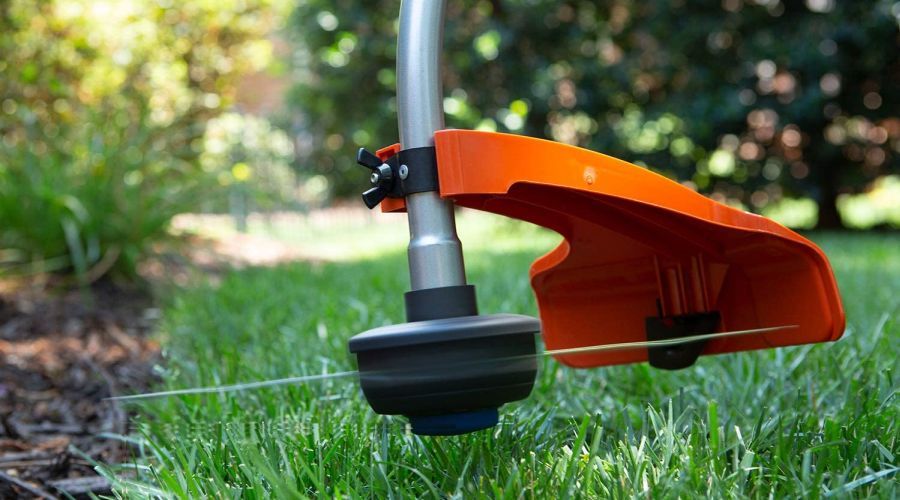 Close-up of a Husqvarna 952711952 string trimmer working on the edge of a garden bed.