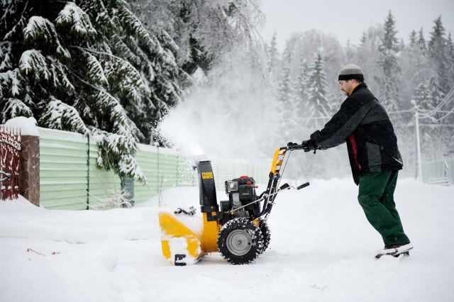 A man is cleaning the country road with snow blower in winter