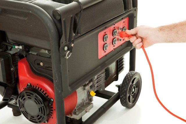 Man's hand plugging an extension cord into an emergency generator.