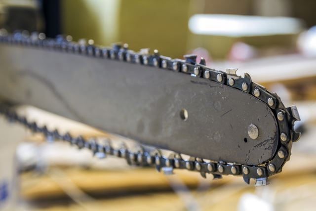 Closeup view of a chainsaw bar and cutting chain at construction site.