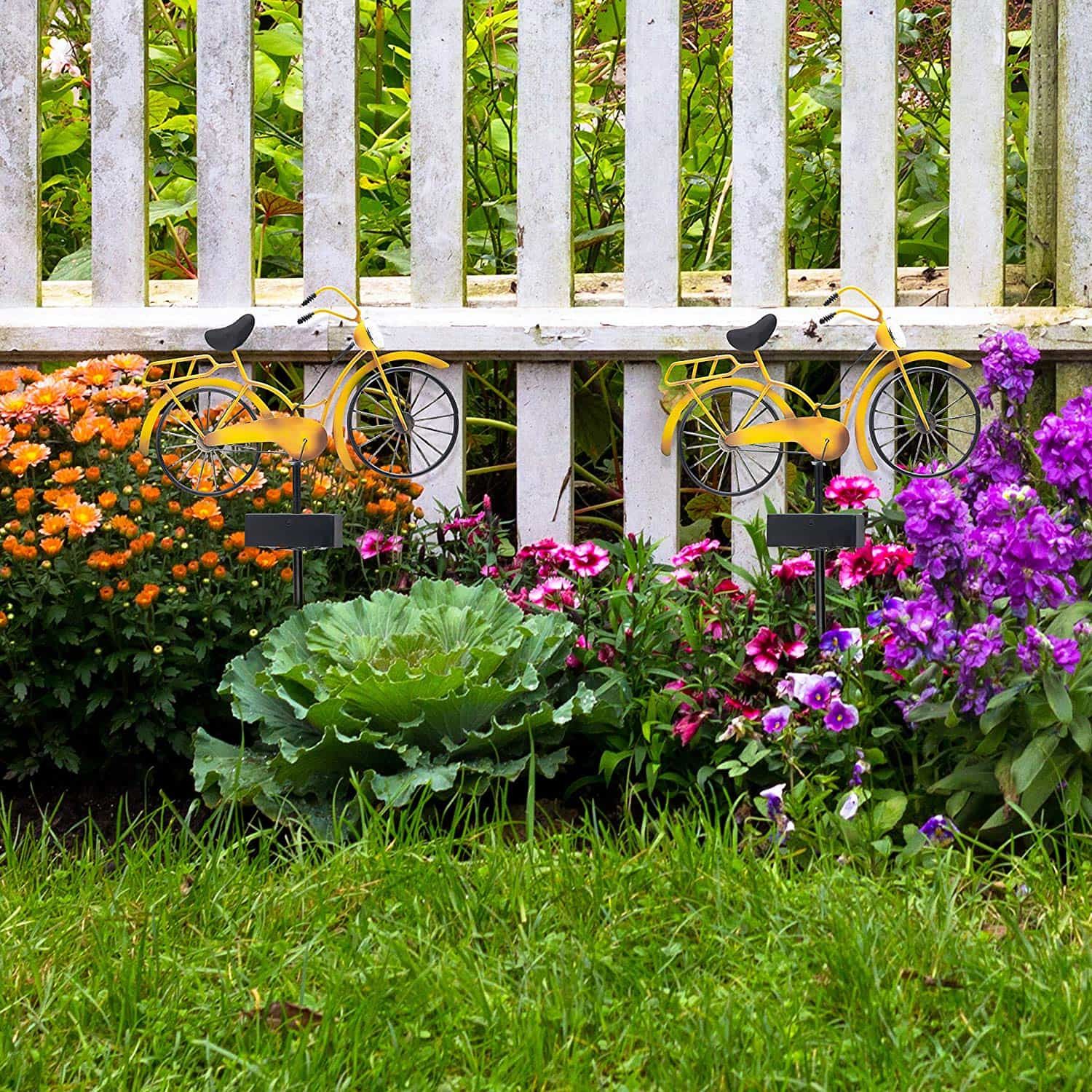 Two little yellow bikes on orange and purple flowers beside the fence