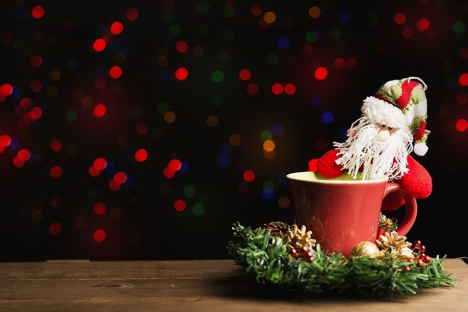 A cute little santa doll on a red tea cup placed on a Christmas wreath