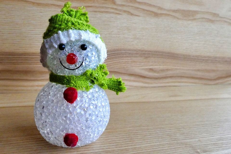 Crystal like body smiling snowman adorned with green cloth as hat and scarf with two red stuff on the body as buttons