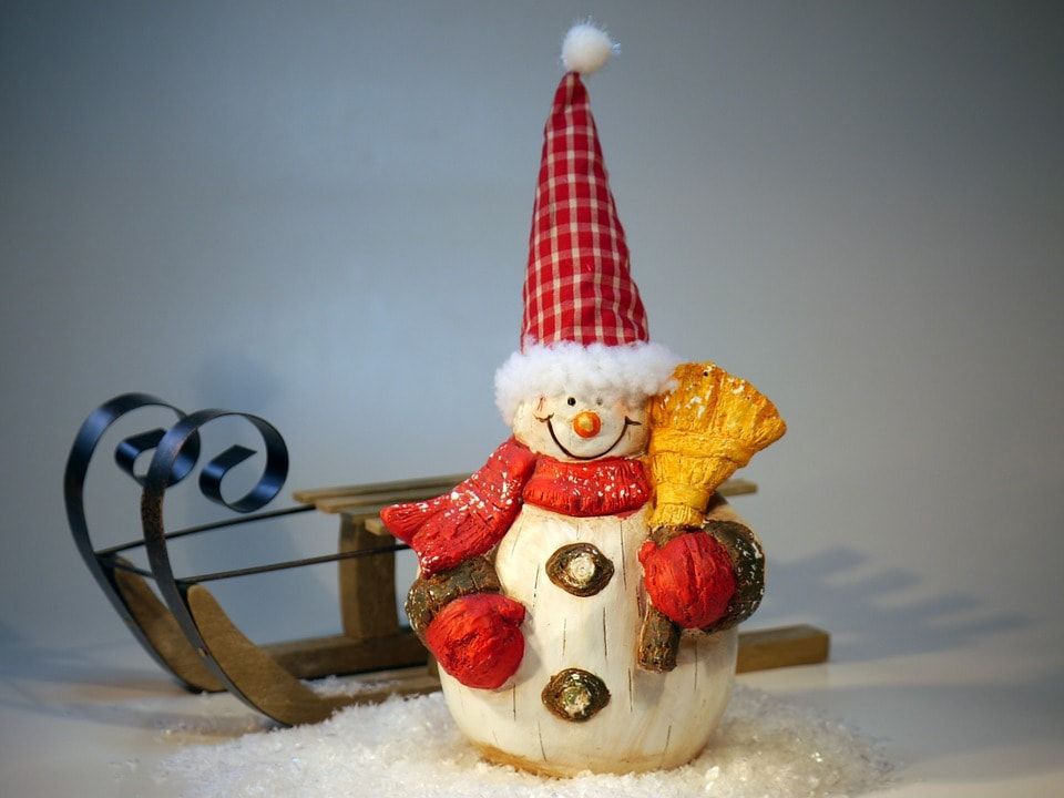 Carved from wood snowman holding a broom with a pointy hat and a sleigh on its background