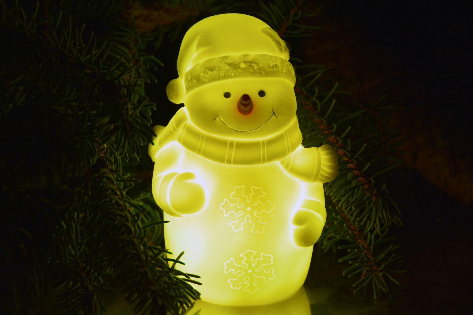 Adorable smiling snowman glowing in a semi golden light with a Christmas tree on its background