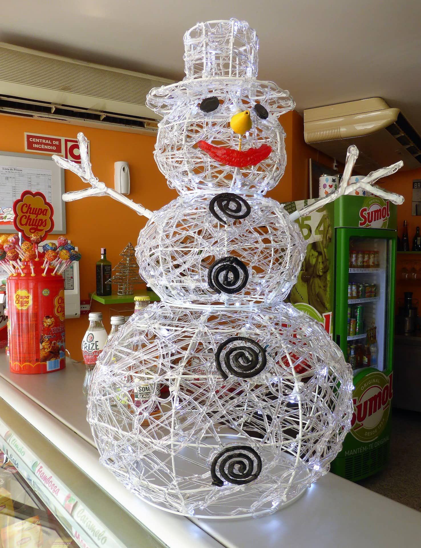 White handmade with wires and lights Snowman standing on a store stall with lollipops on its background