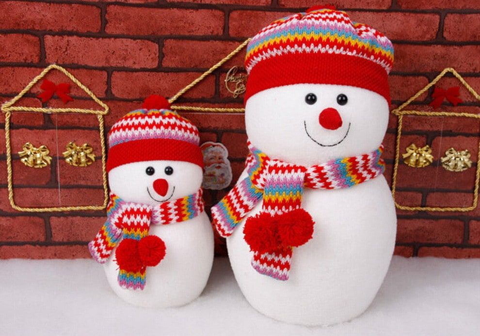 Two snowman standing on a snow wearing colorful and pleasing to the eye hats and scarf with brick wall on the background