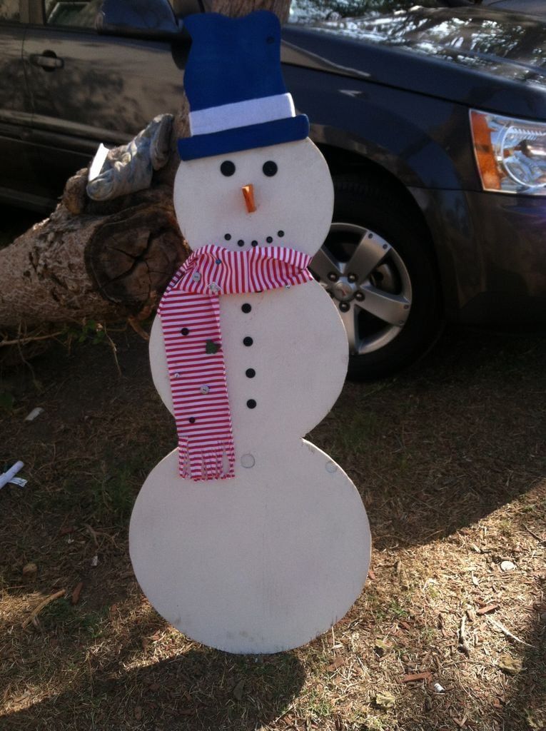 DIY Wooden snowman standing on the ground with a log of tree on its back and a car on its background