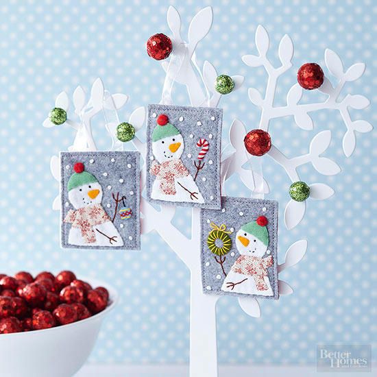 Three cute snowman craft hanged on a white treelike design with green and red balls attached on it as well