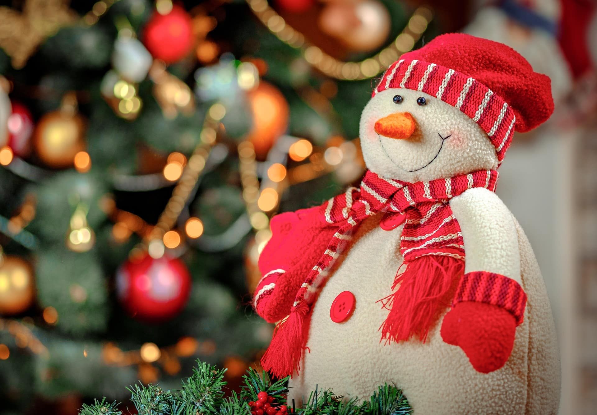 Snowman made of cloth adorned with red hat, scarf and gloves with a blurred christmas tree with decorations on the background