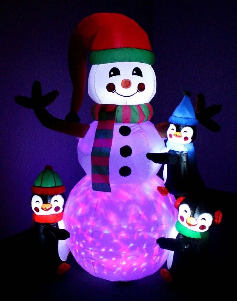 Smiling snowman glowing with lights wearing santa hat with three little plastic penguins hugging it