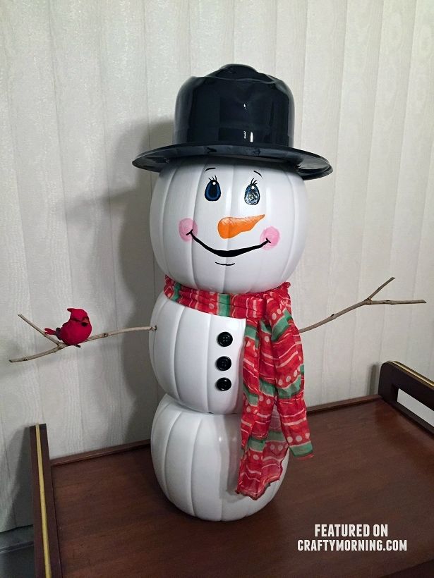 Pumpkins painted with white placed on top of each other to form a snowman figure then adorned with hat and scarf and wooden arm with a drawn eyes, nose and smile
