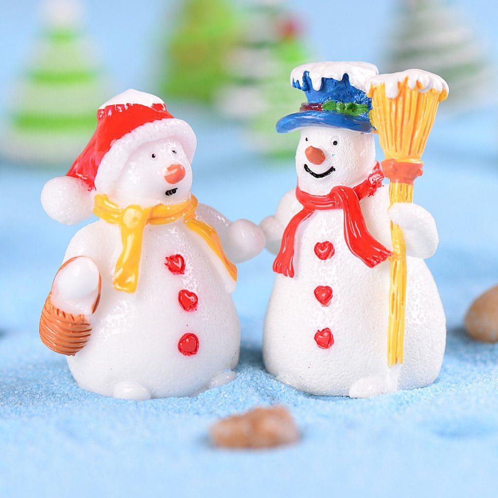 Miniature clay like snowman couple both wearing a hat and heart shaped buttons on their body standing on a light blue sand