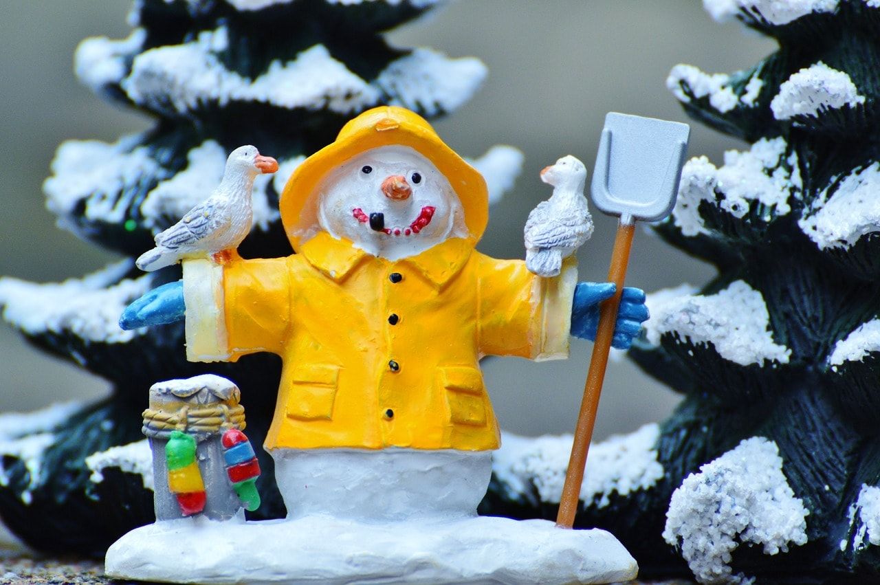Miniature handmade Snowman wearing yellow coat spreading its arms wide having two birds resting in it and holding a shovel in its hands