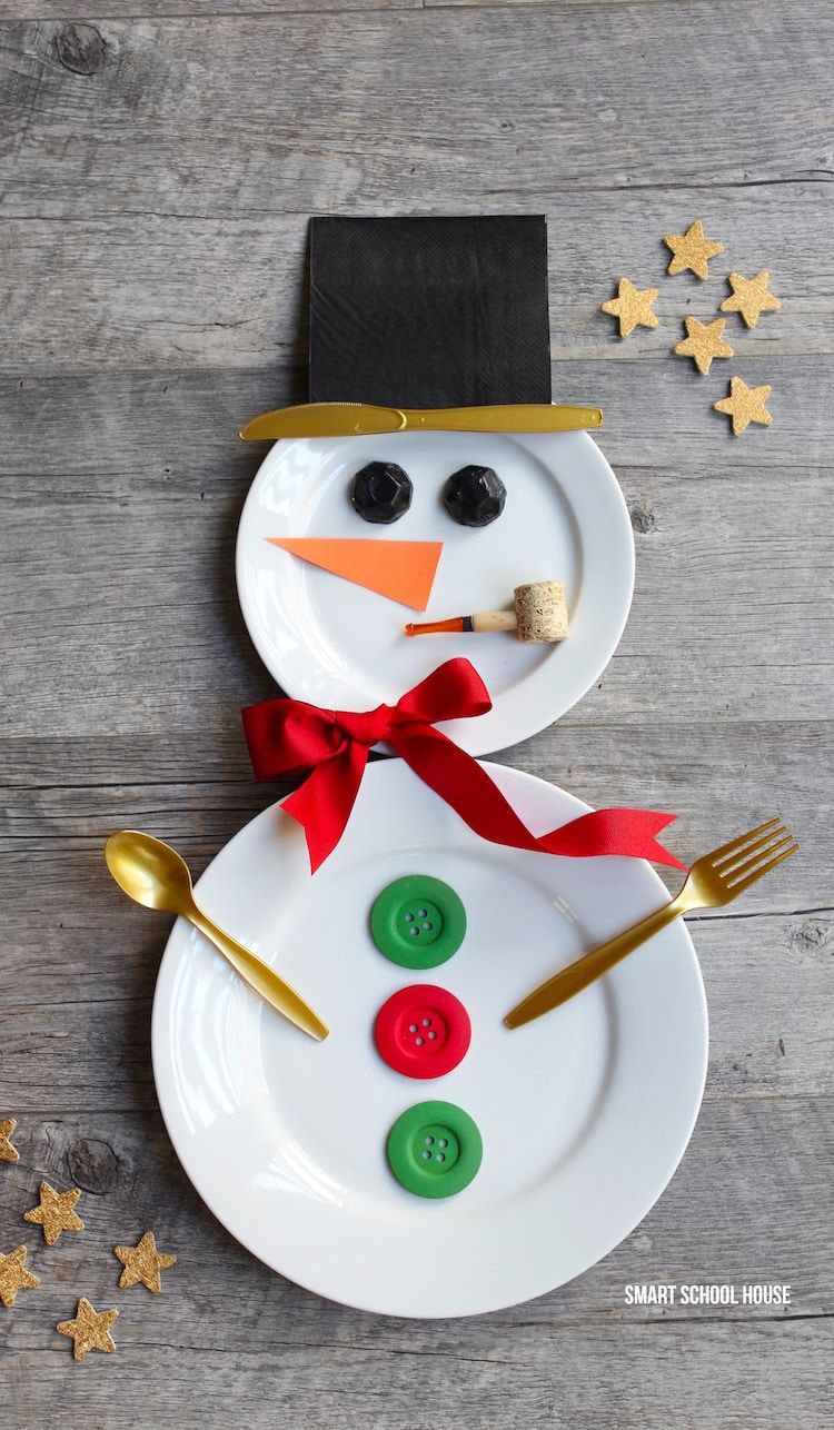 Two plates decorated with ribbon and buttons to look like a snowman using spoon and fork as its arms and knife as part of the hat