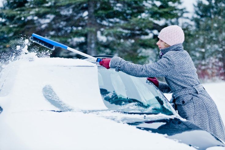 Woman Removing Snow from a Car with a Broom after the Blizzard