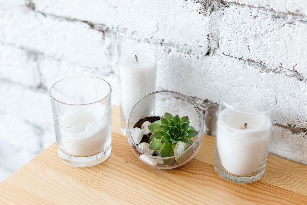 Details of Scandinavian interior design - mini succulent garden in glass terrarium on wooden table, standing near candles on background of white brick wall