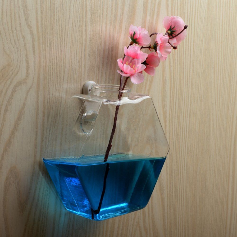 Transparent glass terrarium half filled with blue water with the stem of a pink flower submerged 