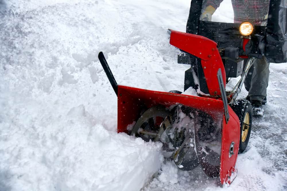 Winter season fun: Man removing snowstorm aftermath with a bright red snowblower.