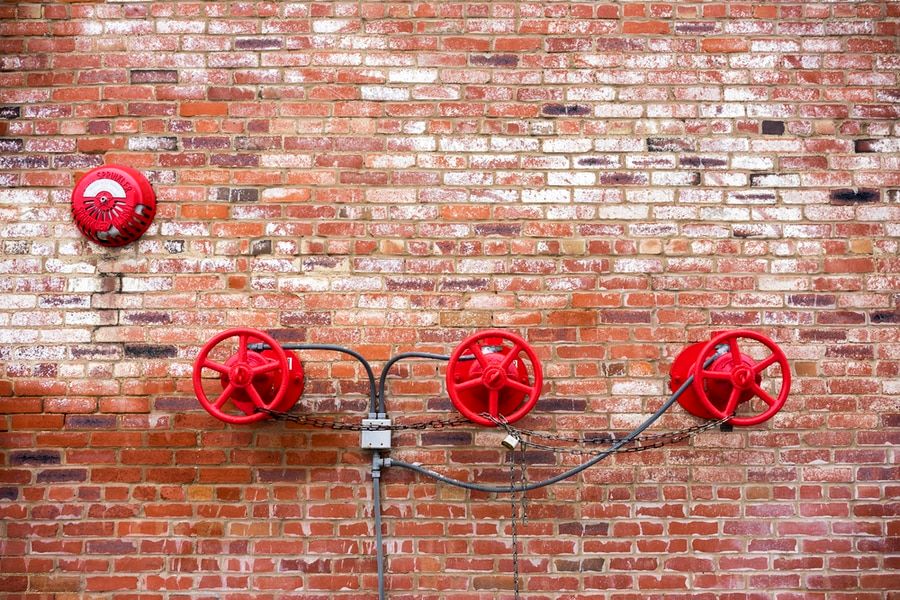 Several red valves connected to one another with brick background