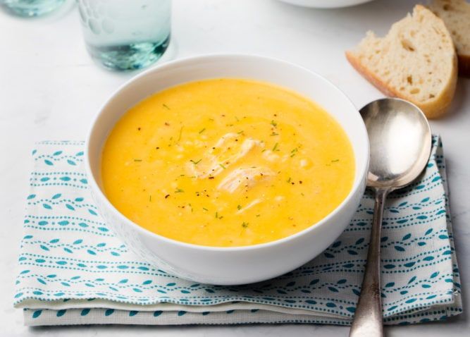 Pumpkin and coconut soup with chicken on white stone background