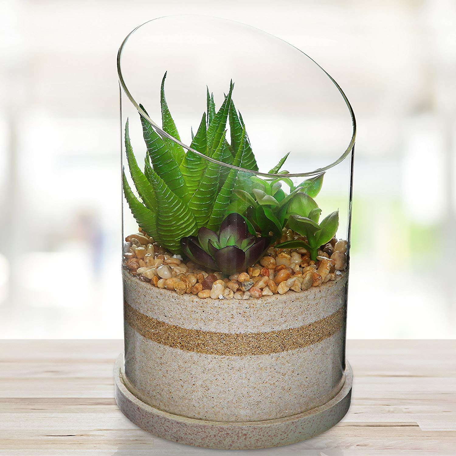 Cylinder shaped terrarium with three layers of sand inside and pebbles with succulents on top of it