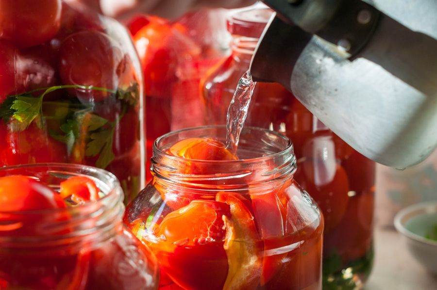 Canning process of tomato in mason jar. On background is few jars with tomatoes. Conservation and cooking.