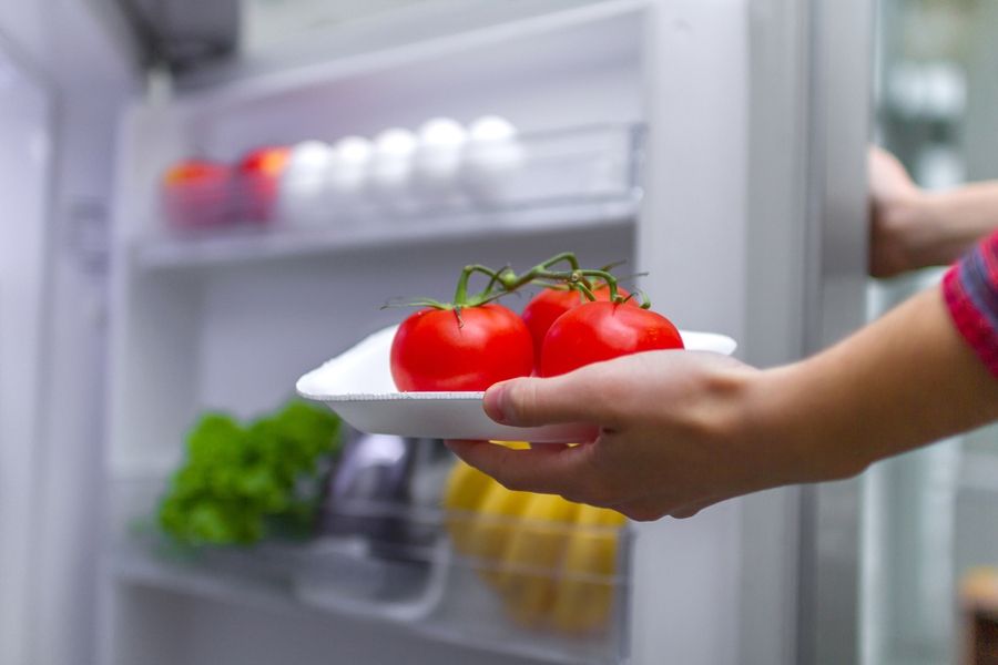 Housewife puts tomatoes in refrigerator. Food storage in the refrigerator. Proper and healthy food. Fresh food and vegetables