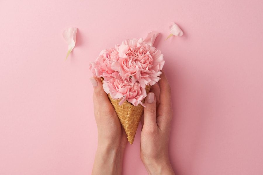 Cropped shot of woman holding wafer cone with beautiful tender flowers isolated on pink