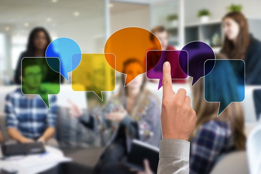 Colorful speech bubbles with a hand pointing to one of it in blurry background of people discussing