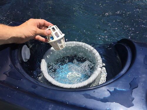 Hand holding a Periodic Products CuLator SpaPak Hot Tub Metal Eliminator and Stain Preventer, placing it to a tub with water