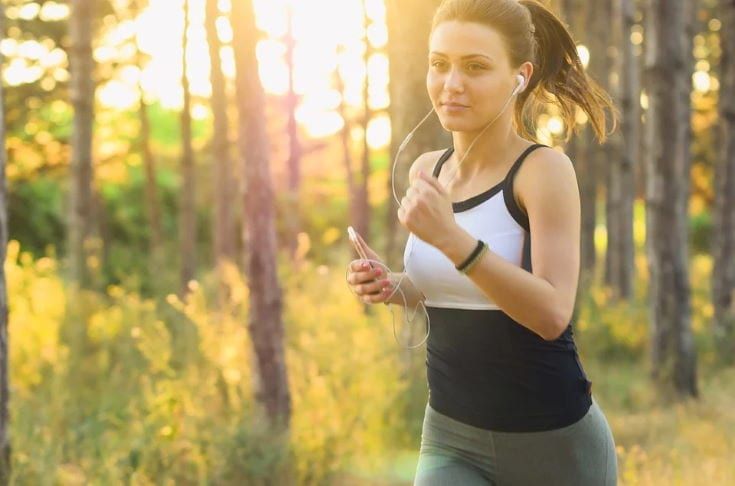 woman running wearing headset in blurry trees background