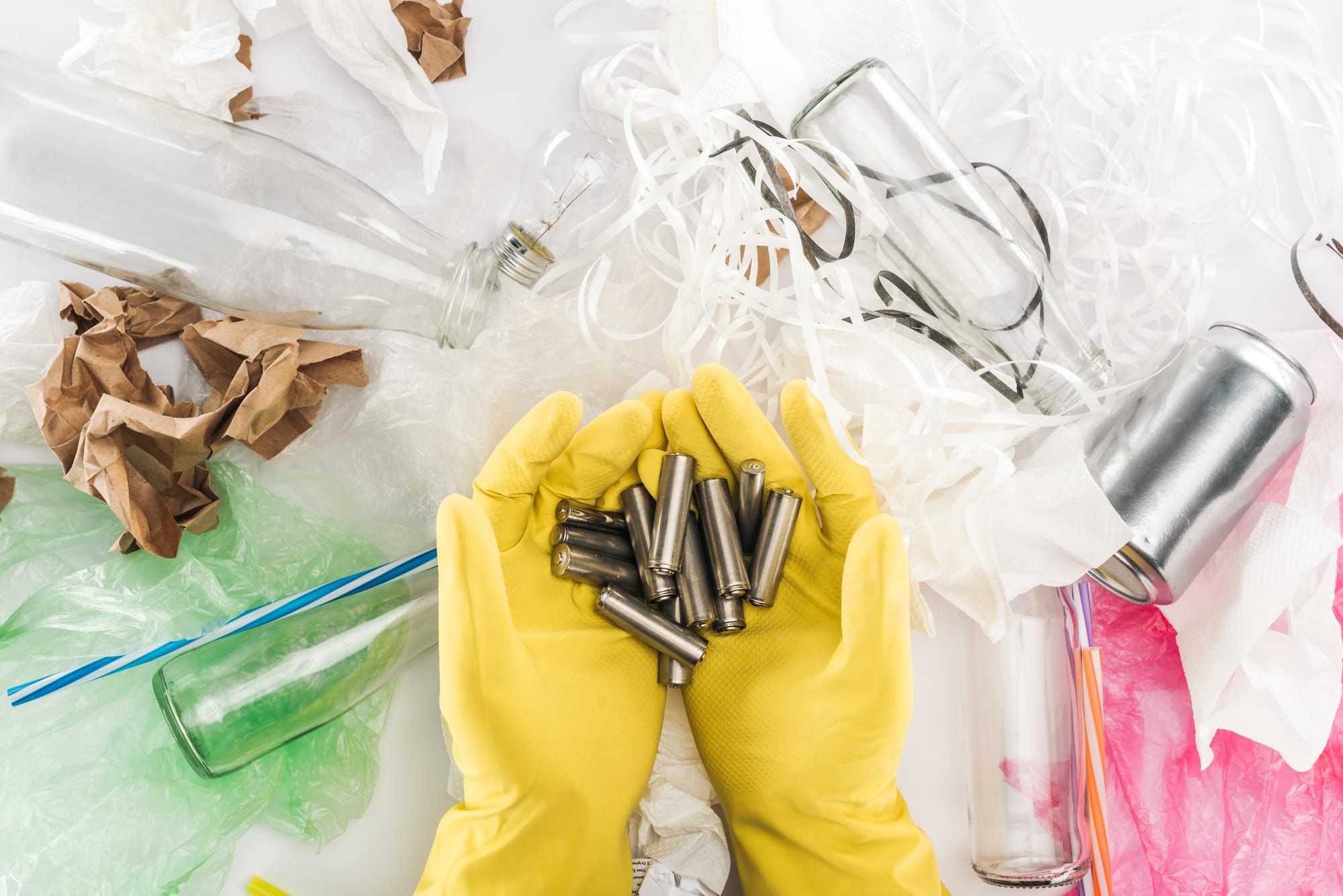 Cropped view of man holding batteries among can, glass bottles, plastic bags, paper strips, paper and plastic tubes