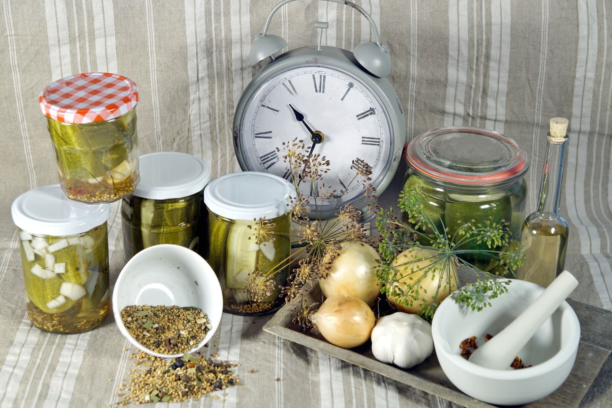 Time to pickled. to keep long time. Pickled cucumbers in glass jar with clock, herbs and dill spices, on a fabric linen background.