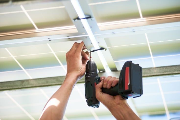 Worker using drill by solar panels installing. Innovative high-tech exterior. Modern solution for natural resources saving, using renewable solar energy. Environment friendly. New technologies.
