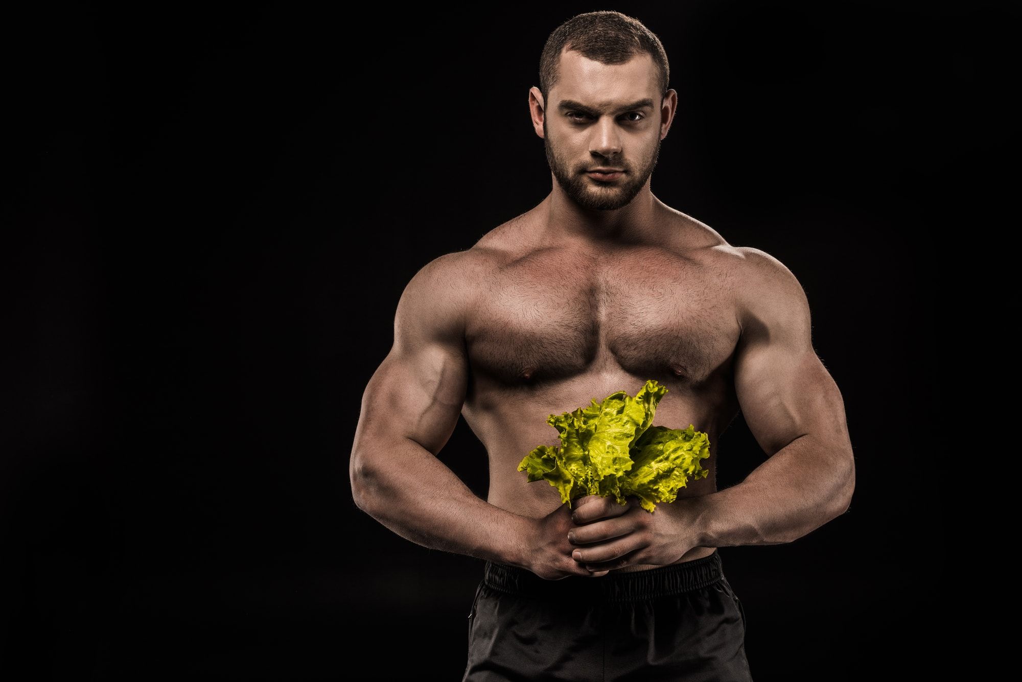 Young confident shirtless sportsman holding Lettuce salad leaves and looking at camera