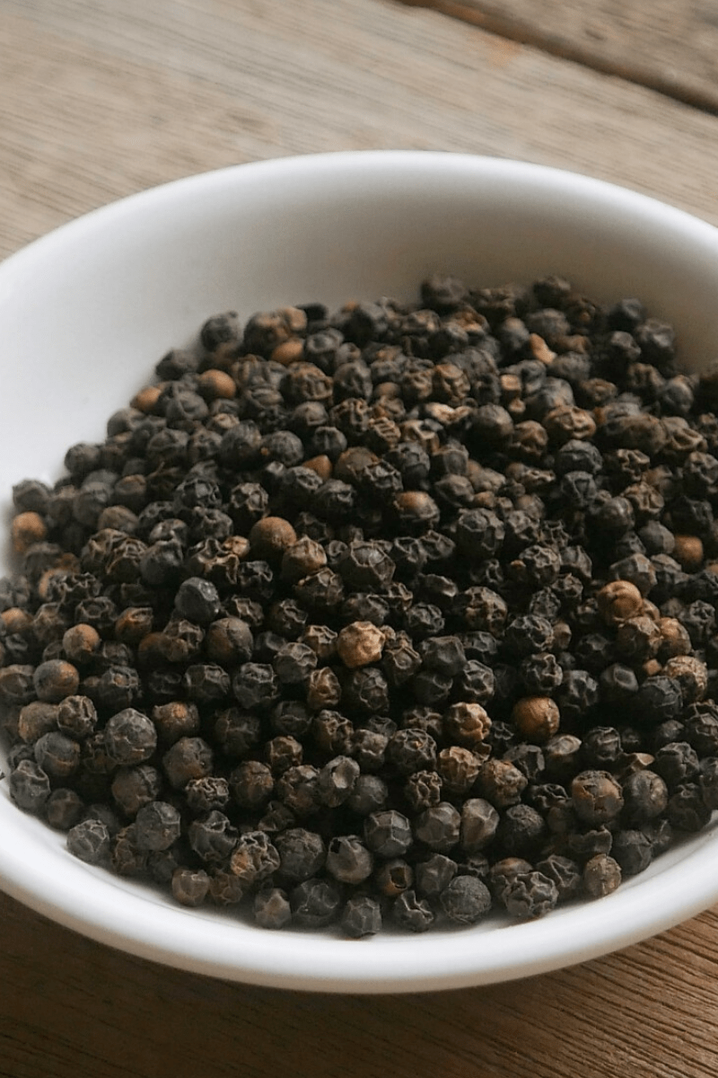 a ceramic bowl of black peppercorns on a wooden table