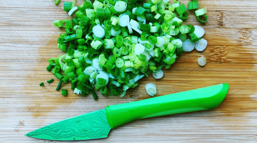 green onions and green knife on wooden cutting board