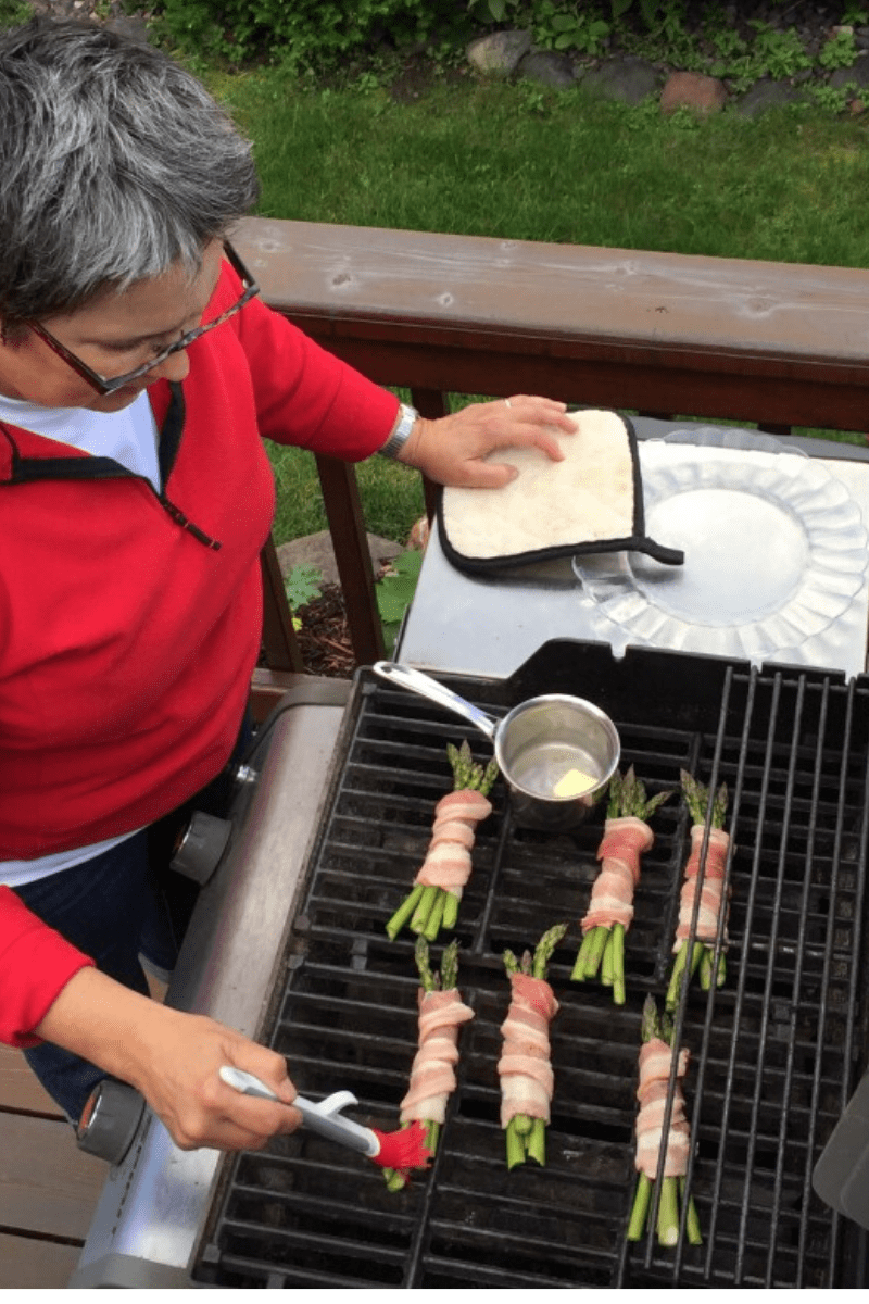 red sweater on woman grilling bacon wrapped asparagus on gas grill outdoors