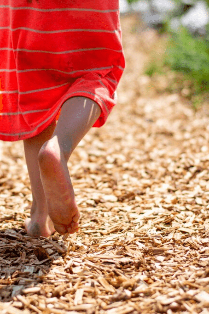 child running barefoot on path covered with wood chips