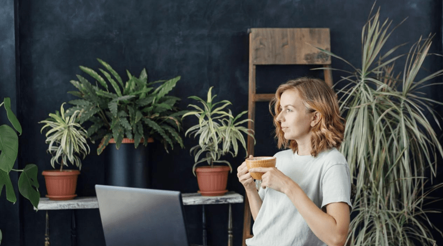 woman in room full of house plants shopping online drinking coffee