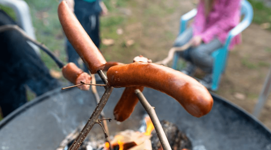backyard bbq hot dog roast on sticks over traditional charcoal kettle grill