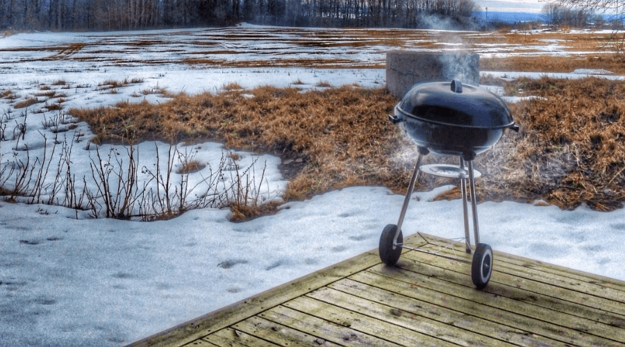 charcoal grill in use in winter on deck with snowy grass