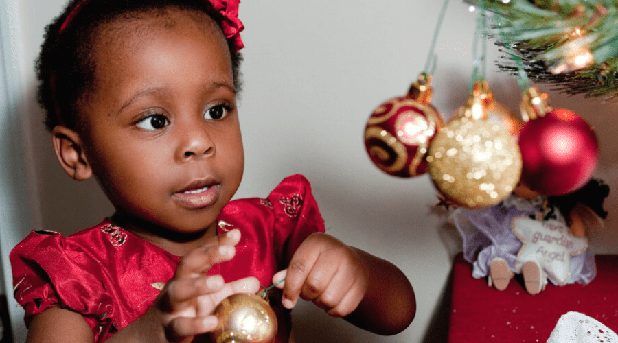 a small girl hangs an ornament to decorate a tree for indoor christmas fun