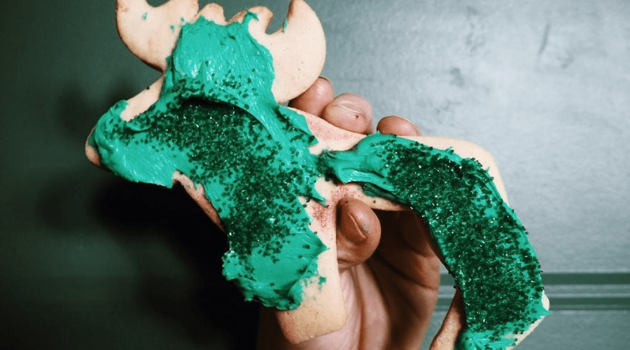 small hand holds a homemade moose cookie decorated with green icing and sugar