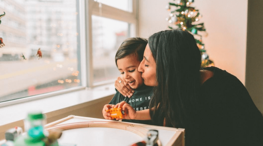 woman kissing son on cheek at home indoors christmas tree in background