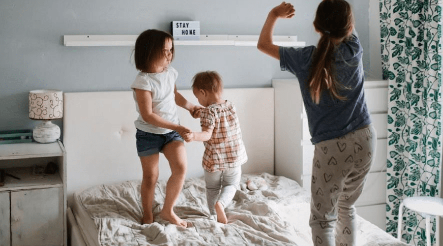 three kids dancing to christmas music on the bed
