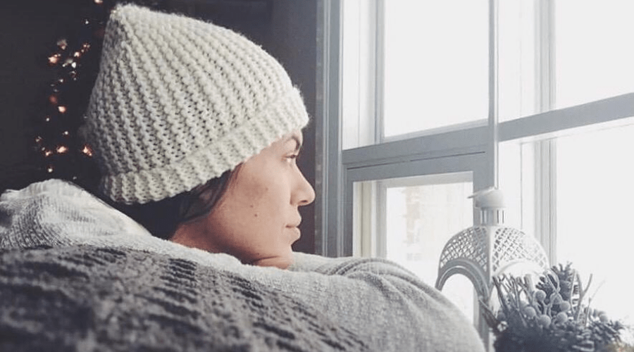woman in knit beanie and sweater staring out of the window