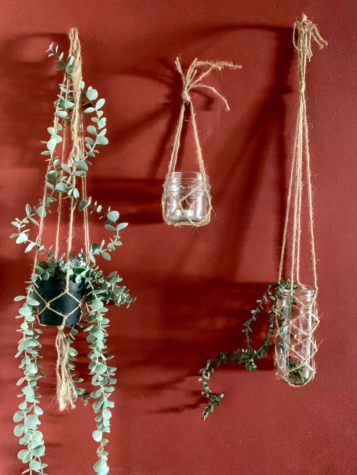 handmade macrame plant hangers on red wall with glass jar planters and succulents