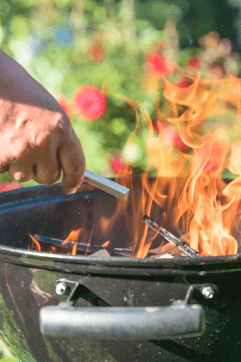 man kindles kettle barbecue in backyard with flowers in background